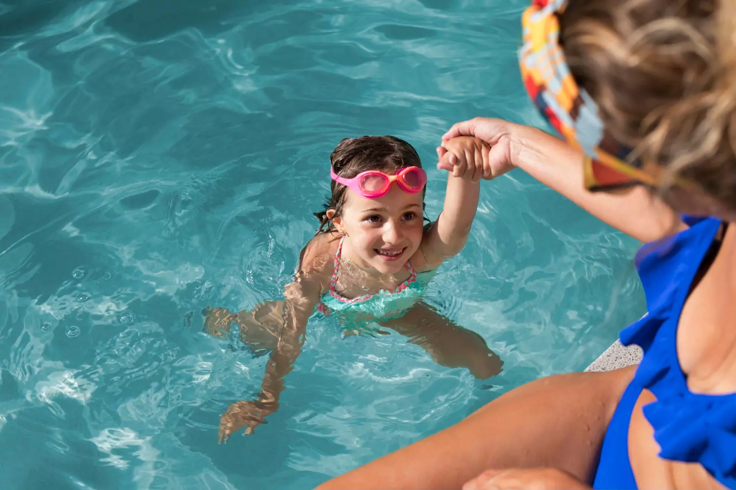 Criança sendo puxada pela mãe em piscina.